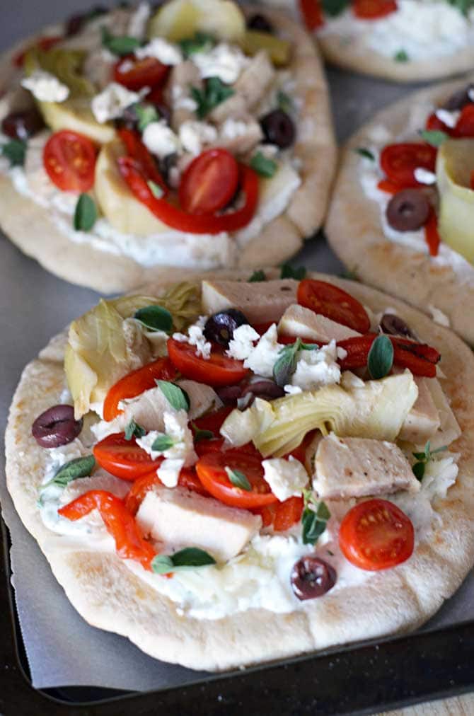 Loaded Greek Chicken "Pitzas".  These pita bread pizzas are topped with tzatziki, chicken breast, 3 cheeses, artichokes, olives, roasted red peppers, and tomatoes.  They're so easy to make and they taste amazing!  The leftovers even taste great cold! | hostthetoast.com