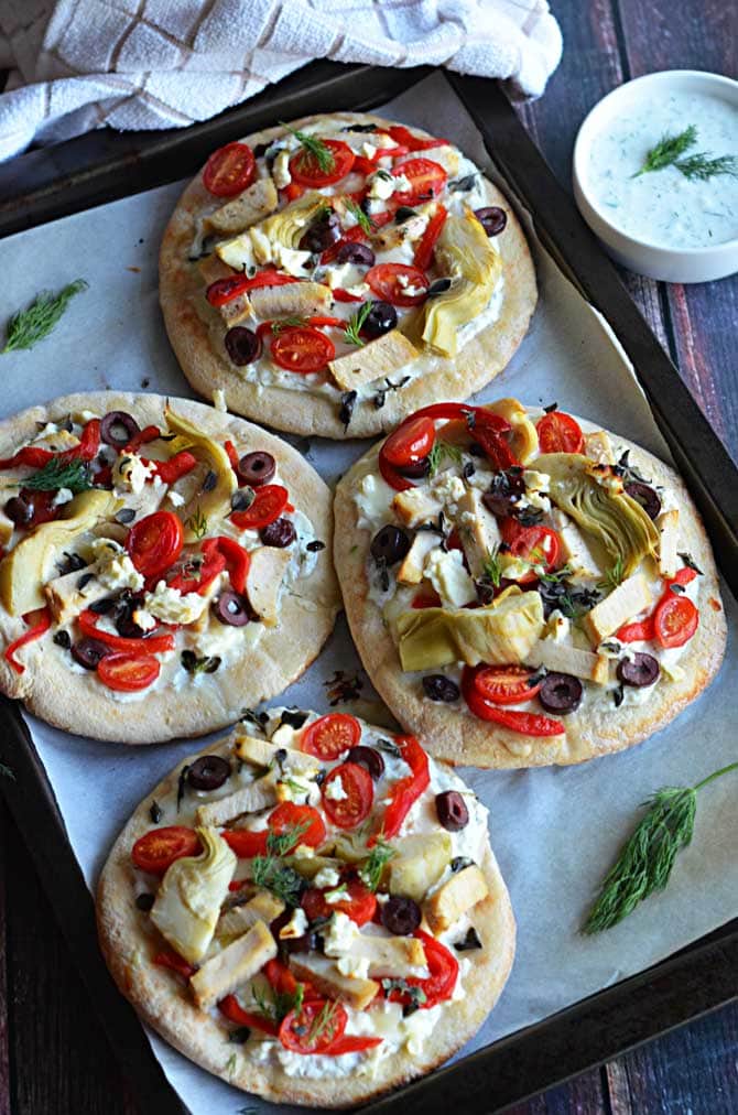 Loaded Greek Chicken "Pitzas".  These pita bread pizzas are topped with tzatziki, chicken breast, 3 cheeses, artichokes, olives, roasted red peppers, and tomatoes.  They're so easy to make and they taste amazing!  The leftovers even taste great cold! | hostthetoast.com