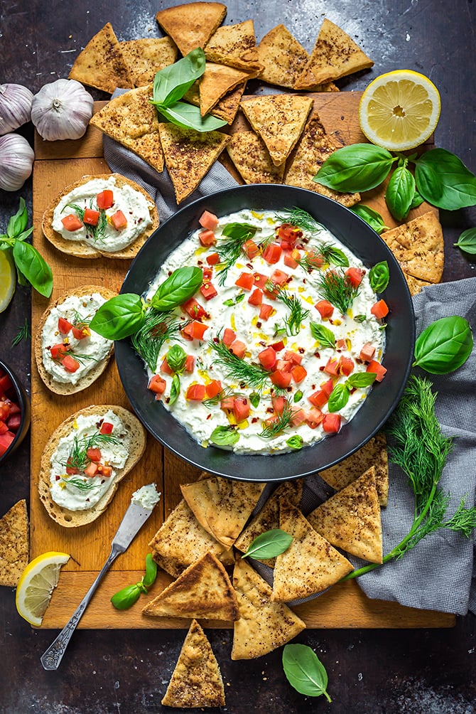 Garlicky Feta Dip in a black bowl on a wooden cutting board surrounded by pita chips and bread.