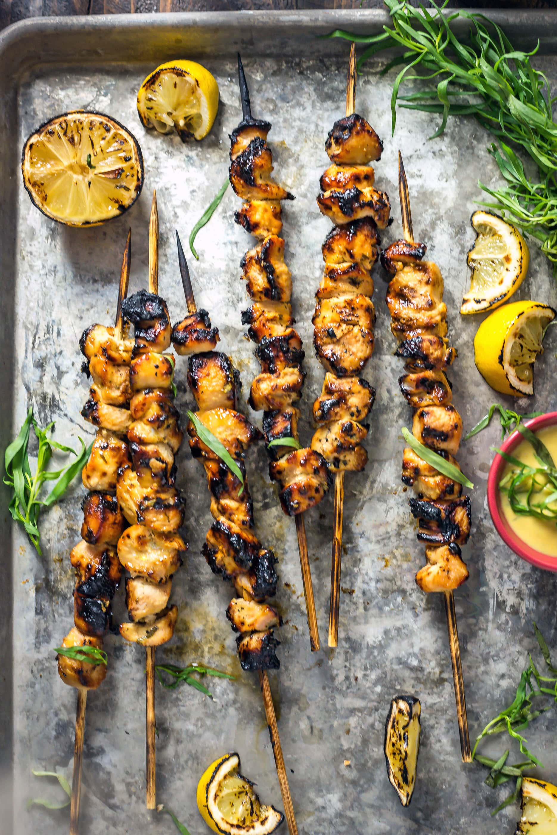 Grilled Tarragon Mustard Chicken Skewers on a baking sheet surrounded by grilled lemons.