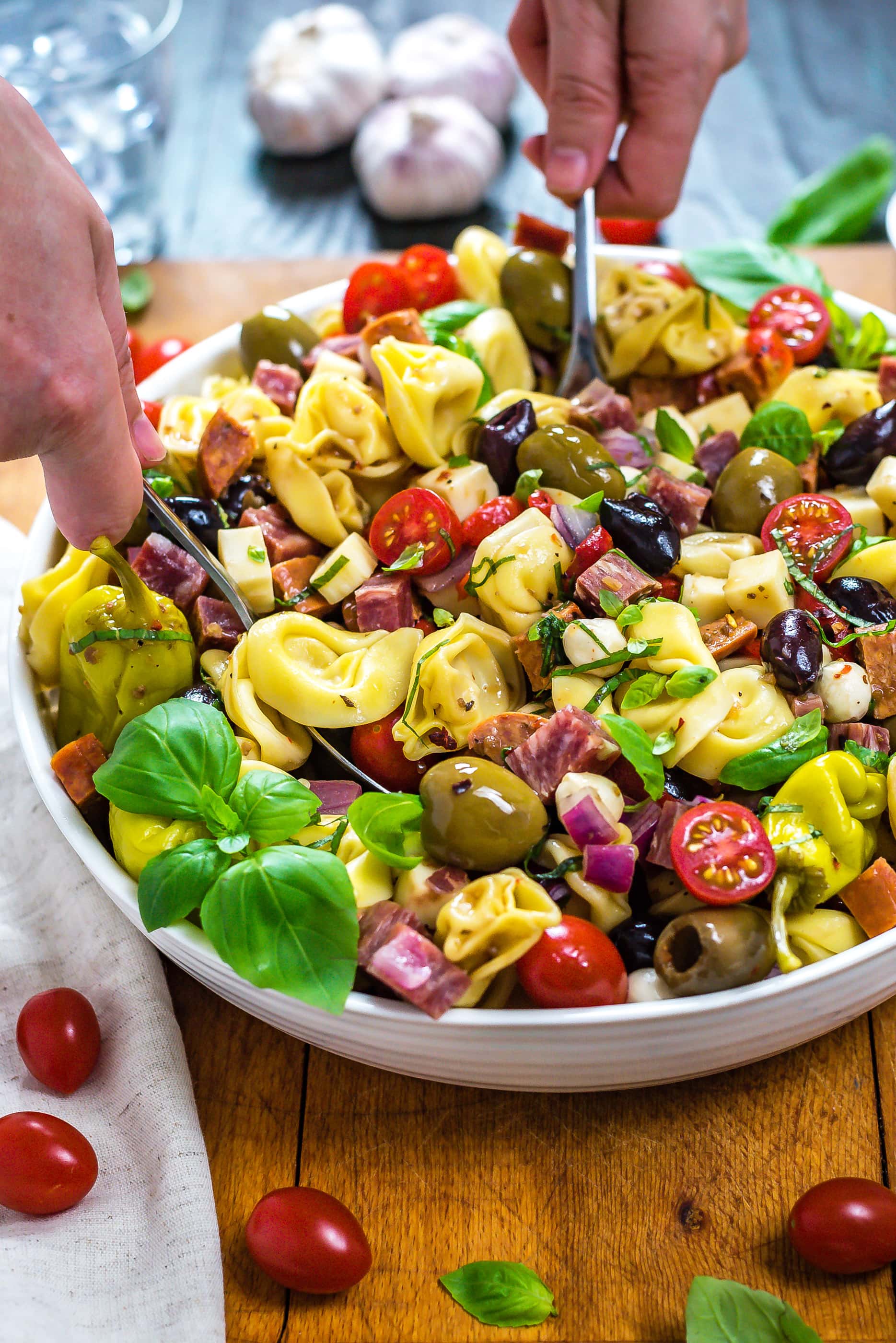 A side view of Antipasto Tortellini Pasta Salad being tossed together in a large bowl.
