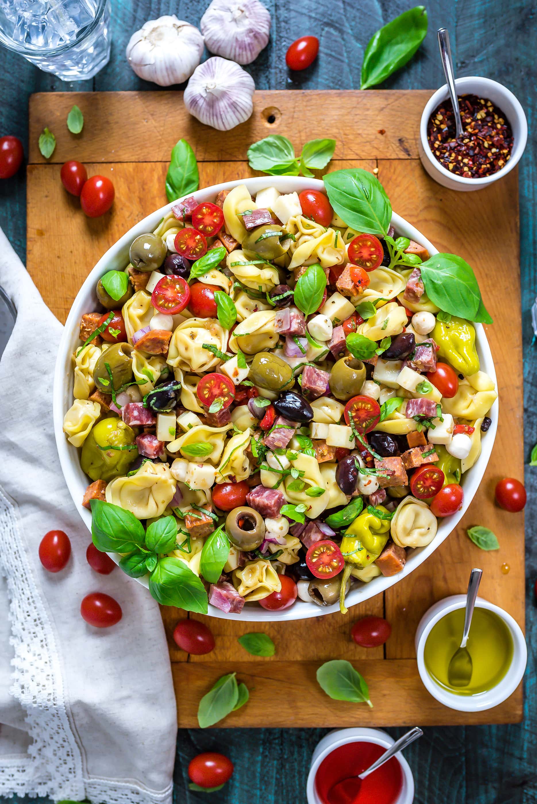 Antipasto Tortellini Pasta Salad in a large white bowl that rests on top of a wooden cutting board.