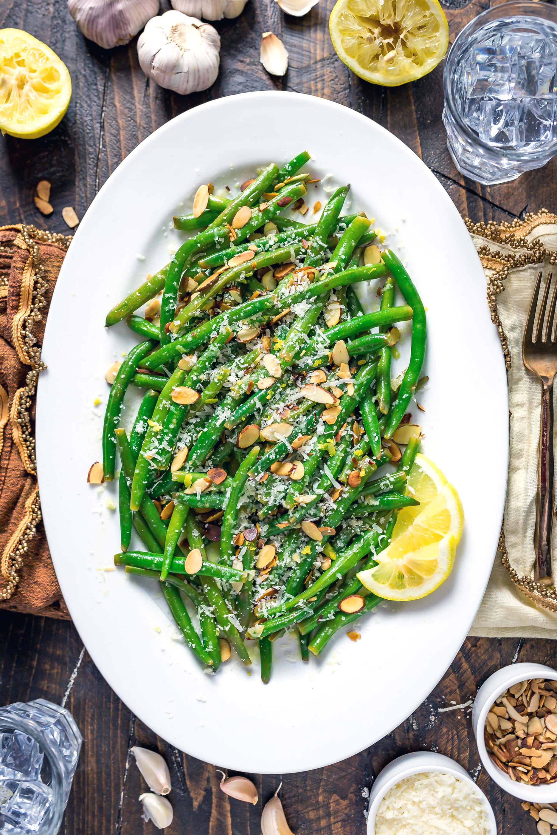 Browned Butter Lemon-Garlic Green Beans on a white plate with sliced lemon, almonds, and parmesan.