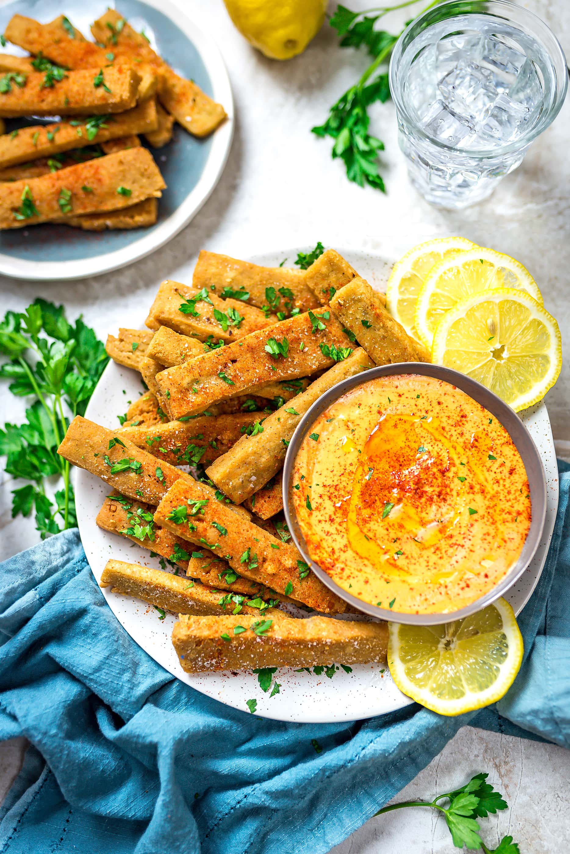 Hummus Fries with Spicy Tahini Dip on a round, white plate with lemon slices.