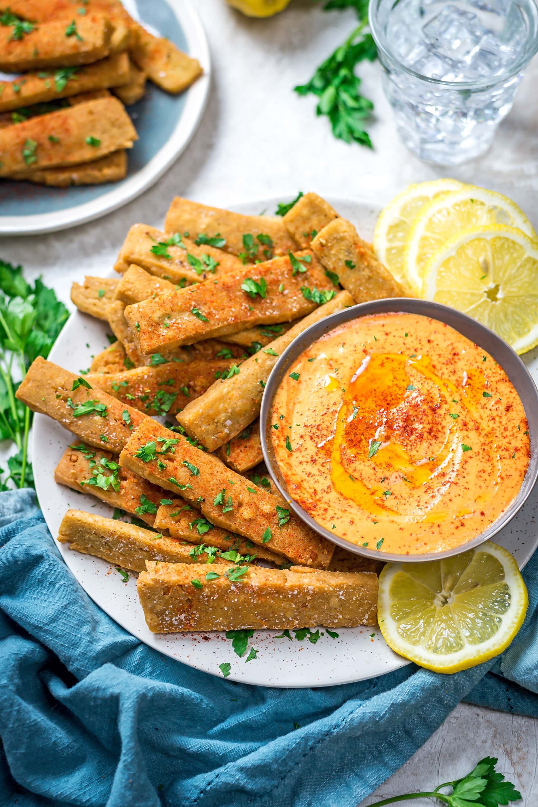 Hummus Fries with Spicy Tahini Dip on a round, white plate with a blue cloth below.