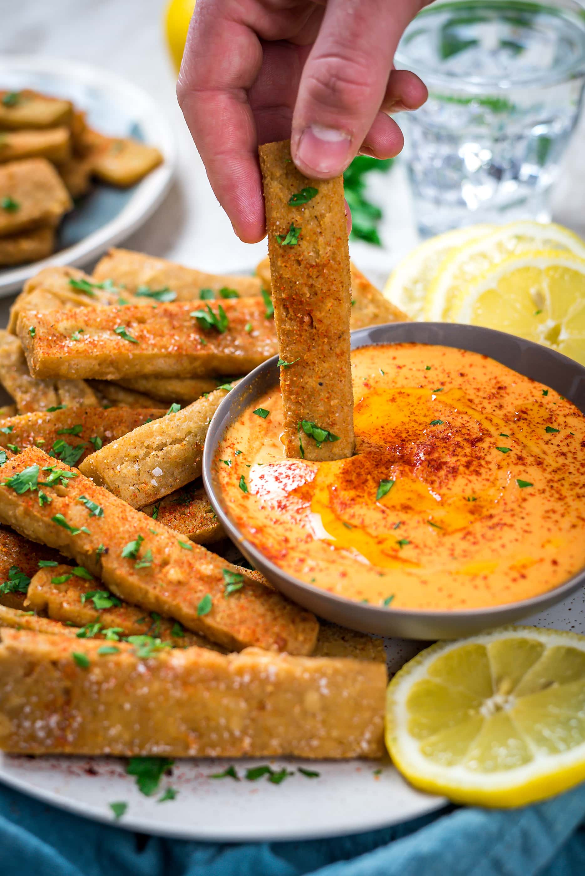 A hand dipping a Hummus Fry into Spicy Tahini Dip. 