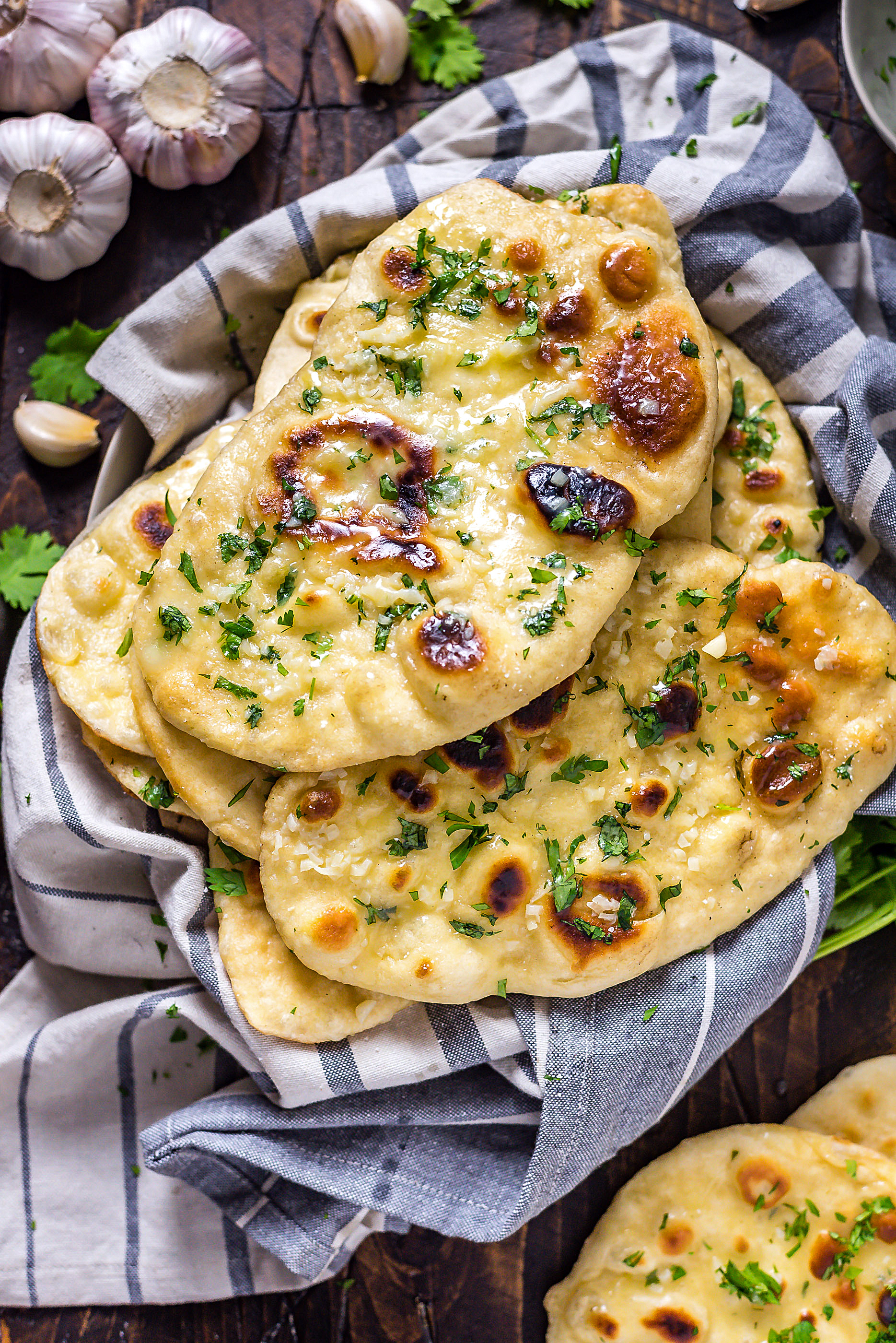 Homemade Garlic Naan sprinkled with cilantro, on top of a striped blue and white towel.