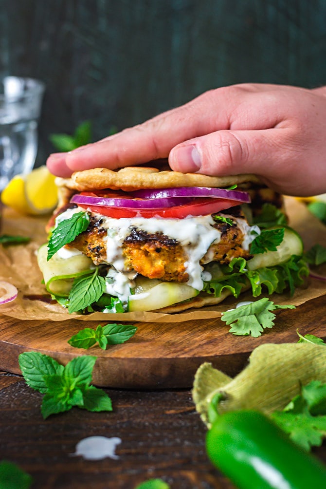 A hand pressing the naan bread down on top of Grilled Tandoori Chicken Patties with Jalapeno-Mint Yogurt Sauce.