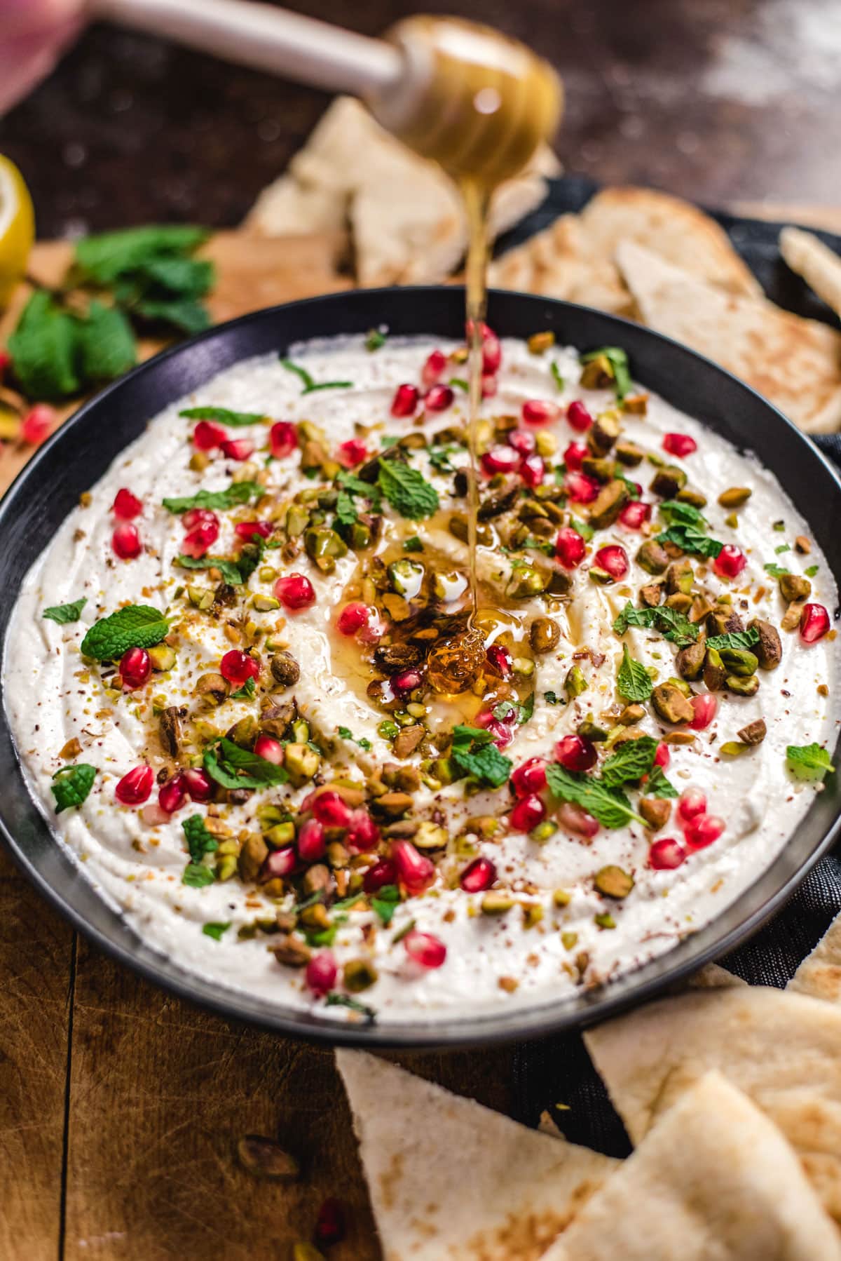 A hand holding a honey stick drizzles honey over a bowl of Honey-Whipped Feta Dip.