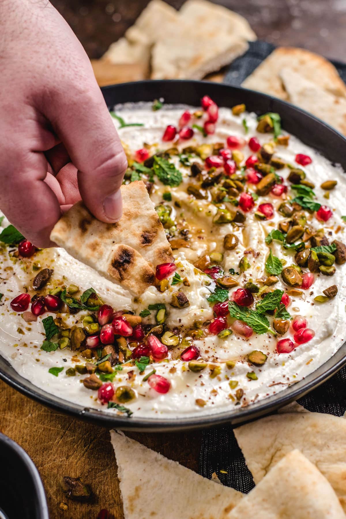 A hand dips a triangle of pita bread into a bowl of Honey-Whipped Feta Dip. 