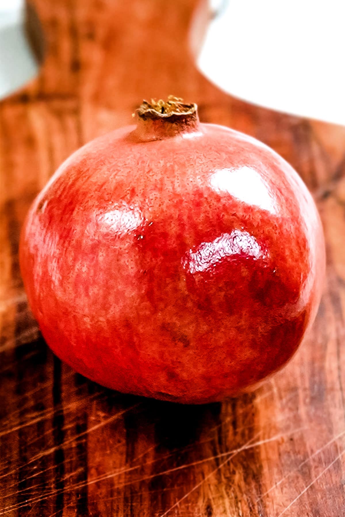 An in-tact pomegranate on a wooden cutting board.