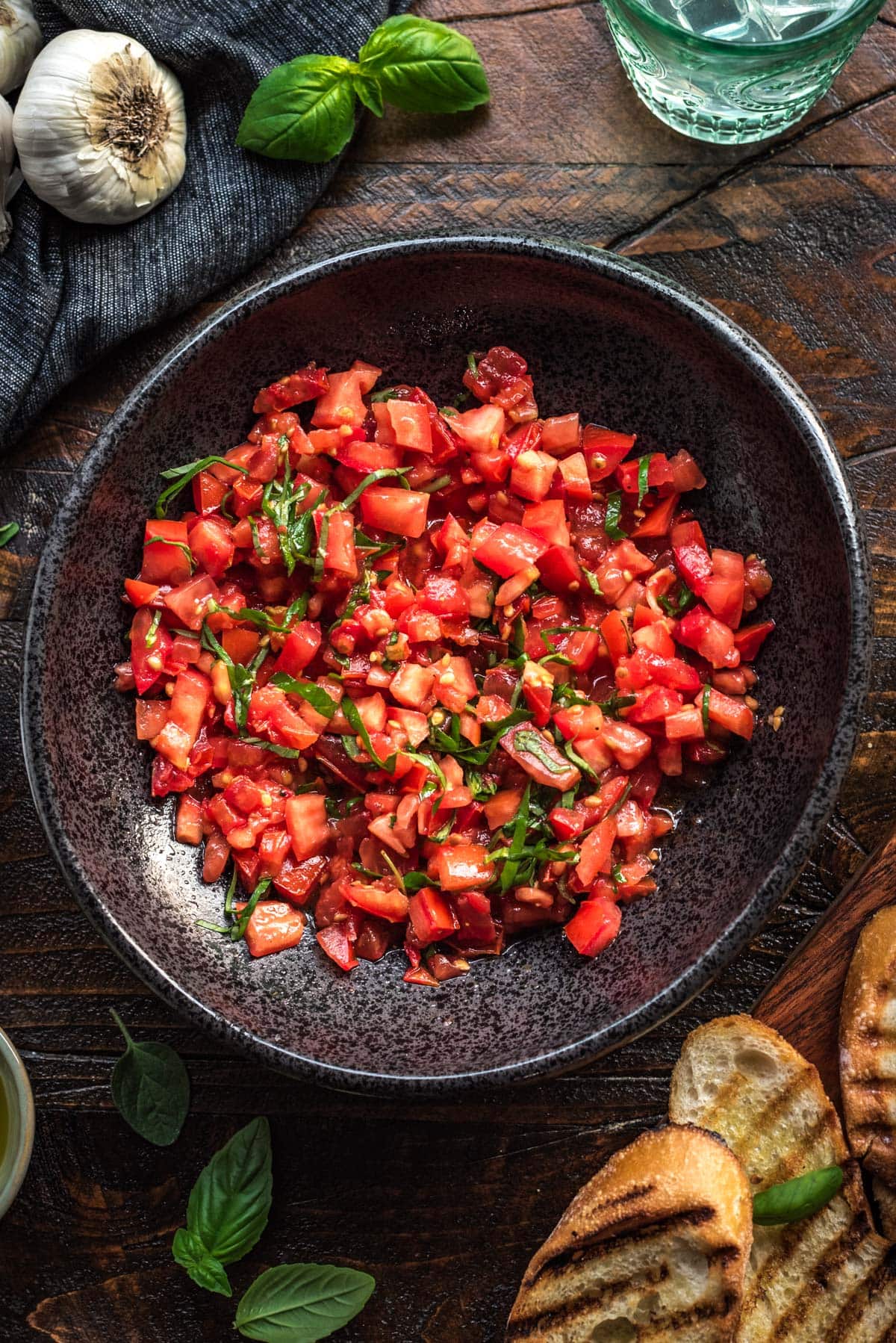 A large black bowl filled with a vibrant chopped tomato and basil mixture, with grilled bread on the side.