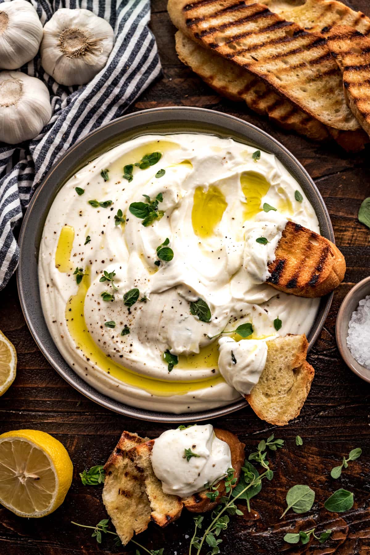 Pieces of crusty toasted bread dipped in whipped ricotta, resting atop a gray bowl filled with whipped ricotta dip.