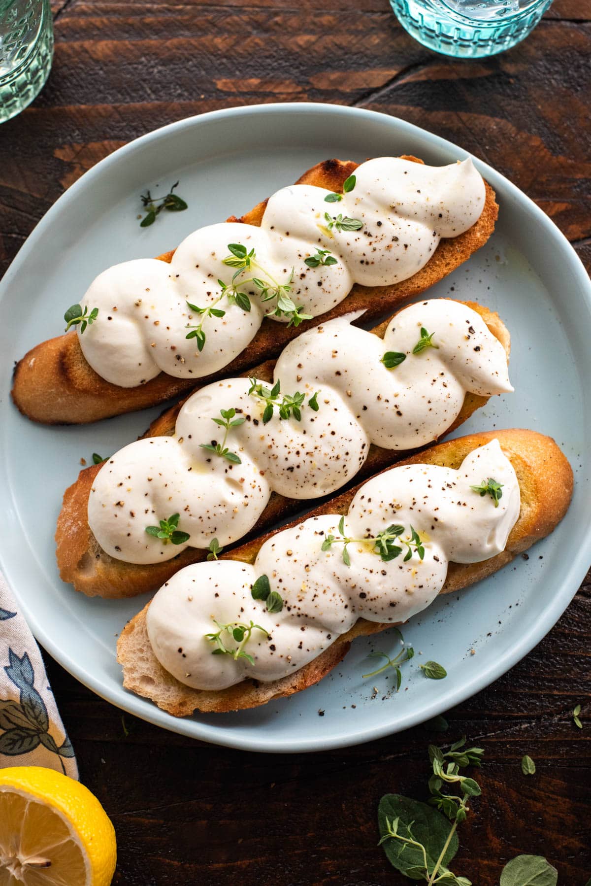 Three pieces of bruschetta toast, topped with piped whipped ricotta and resting on a light blue plate.