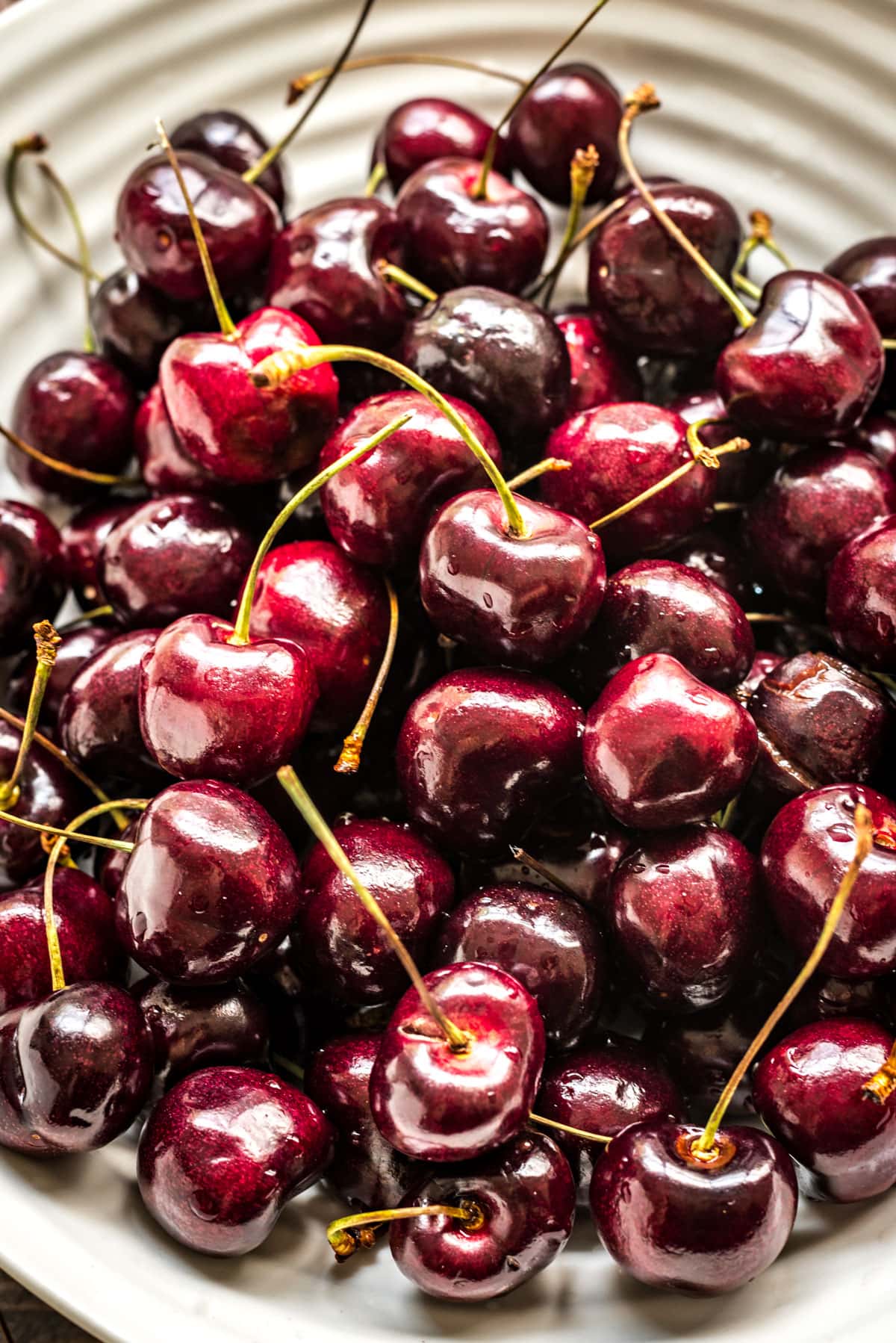 A closeup view of a white ceramic bowl filled with dark fresh cherries.