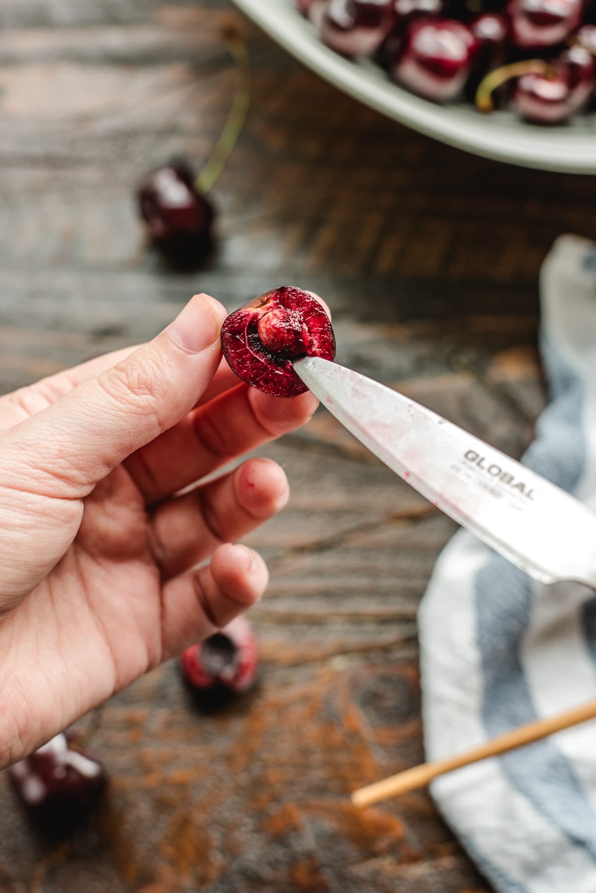 A pairing knife with the tip stuck below a cherry pit to remove it.