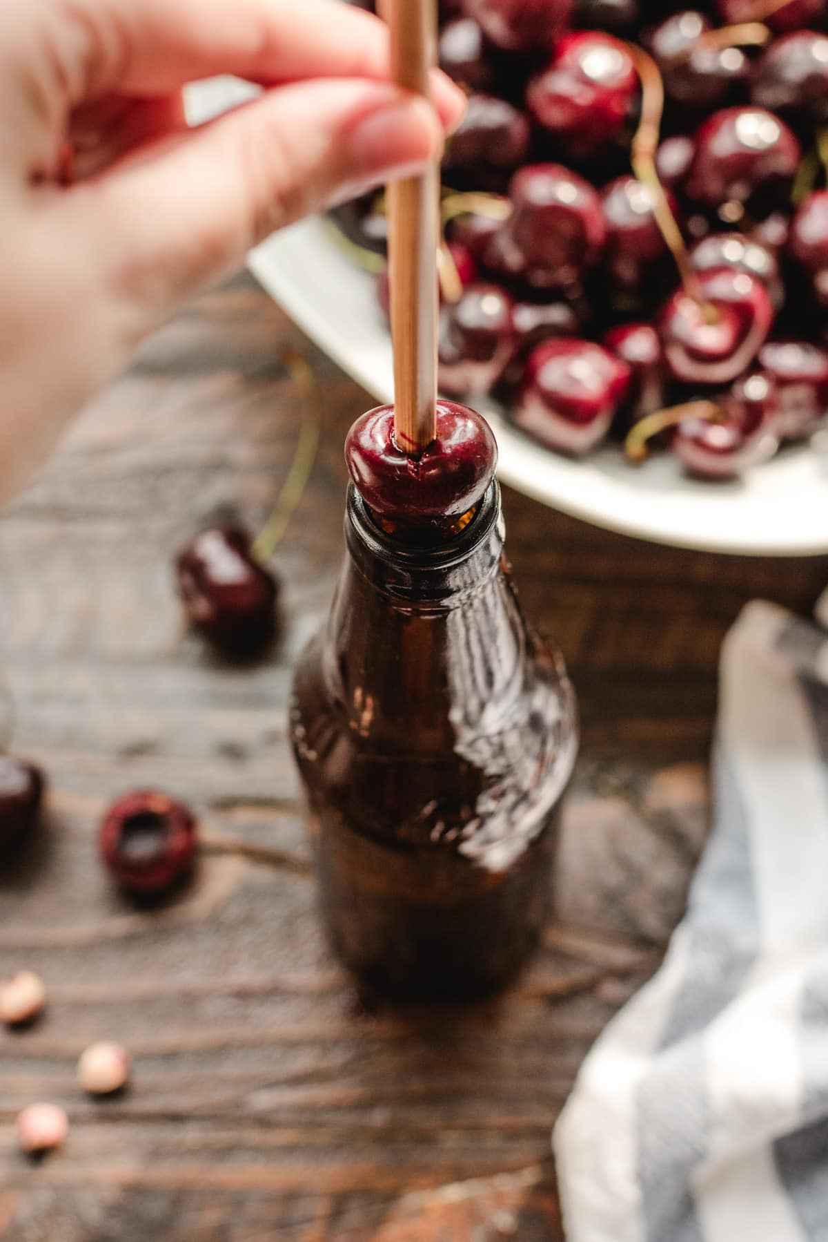 A chopstick being pushed into the center of a cherry which is placed over an empty beer bottle.