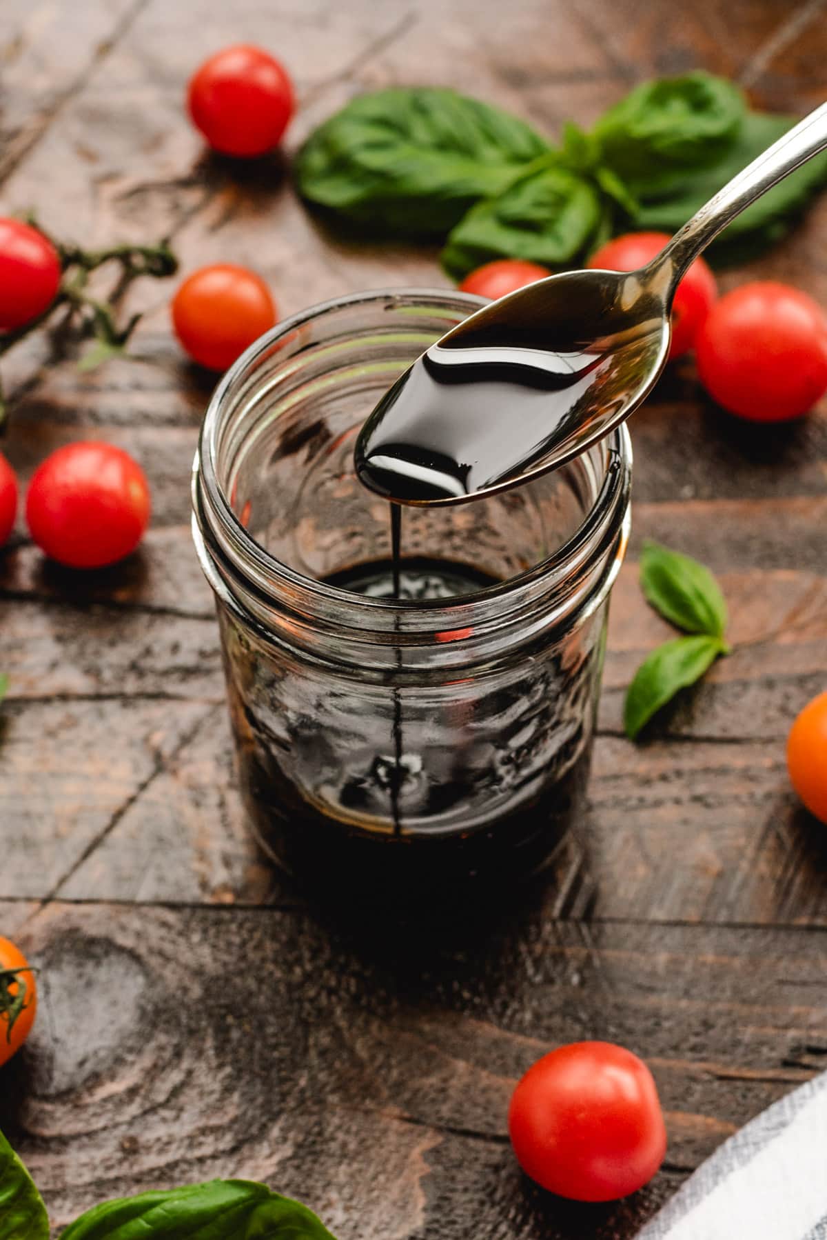 A spoon of thick balsamic glaze drizzling into a glass jar.