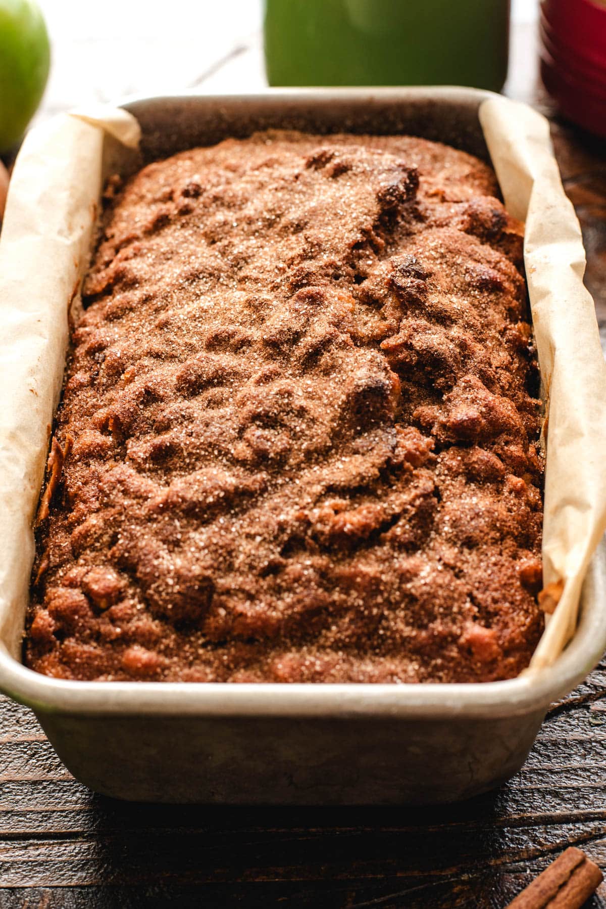 Cinnamon-sprinkled apple bread in a large loaf pan lined with parchment paper.