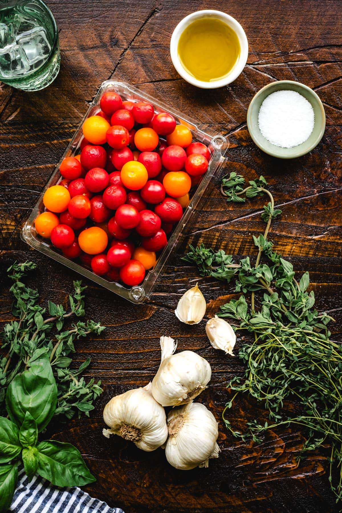 Ingredients for roasted tomatoes including assorted cherry tomatoes, olive oil, salt, garlic, oregano, thyme, and basil.