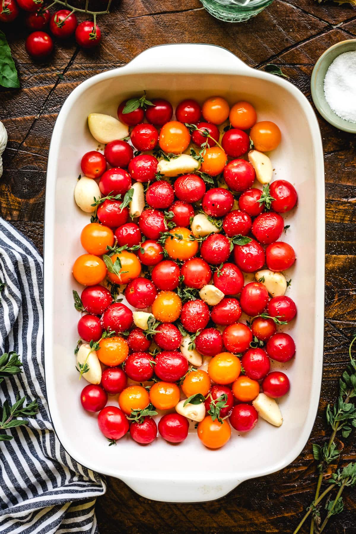 Cherry tomatoes, garlic cloves, fresh herbs, oil, garlic, salt and pepper in a baking dish to be roasted.