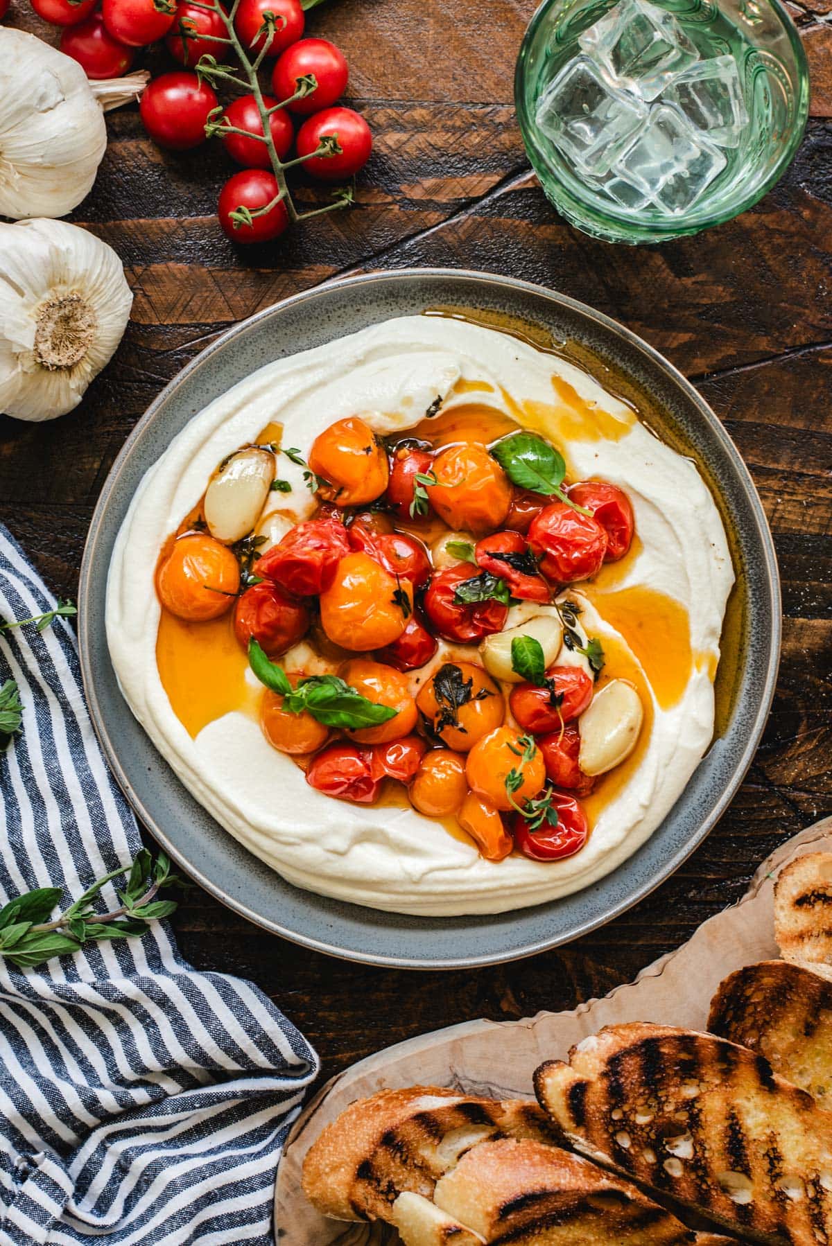 Roasted cherry tomatoes, galric, and herbs over a plate of whipped ricotta to be served as a dip.