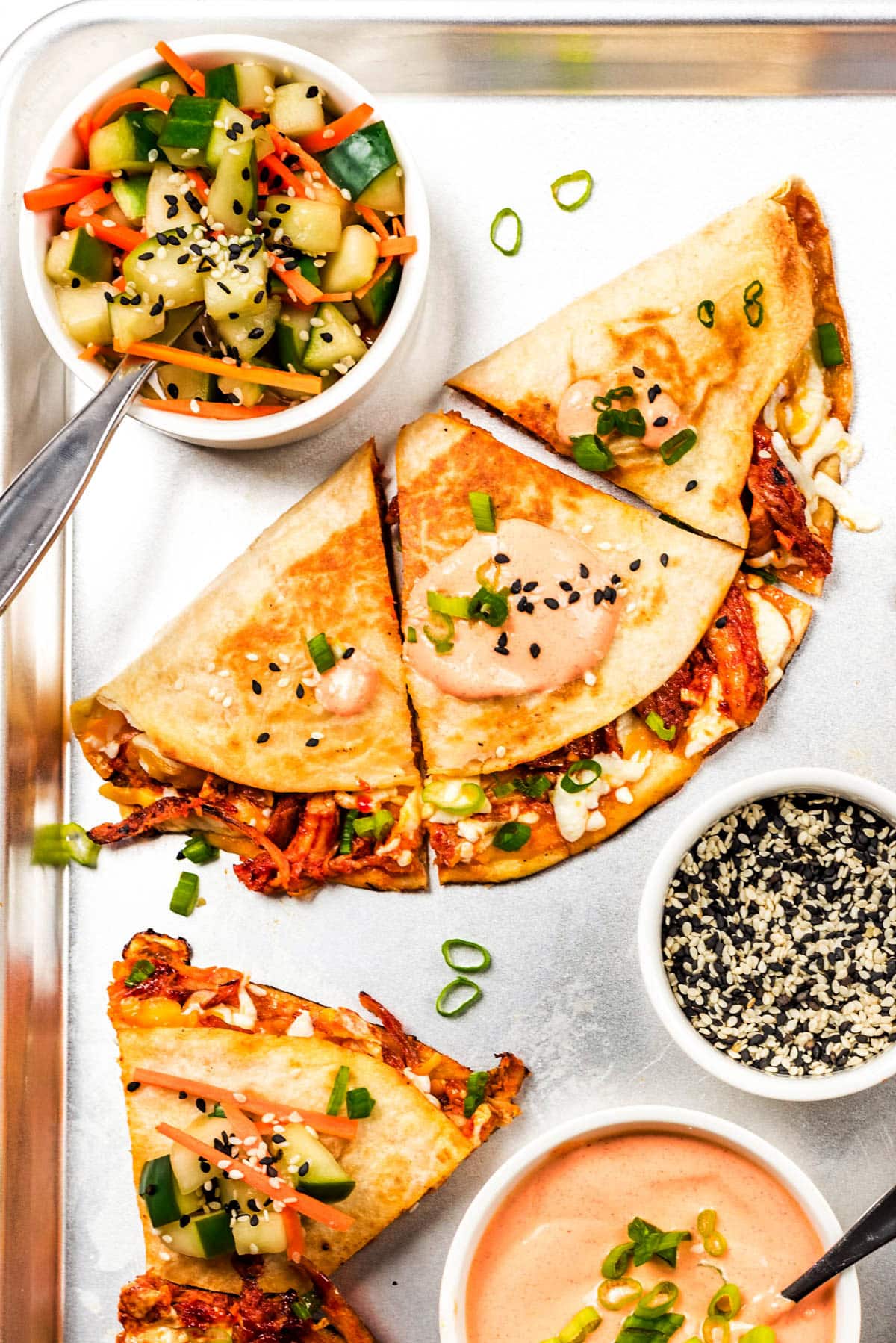 A quesadilla loaded with gochujang glazed shredded chicken, melted cheese, and green onion, cut into thirds and served with crema and pickled vegetables.
