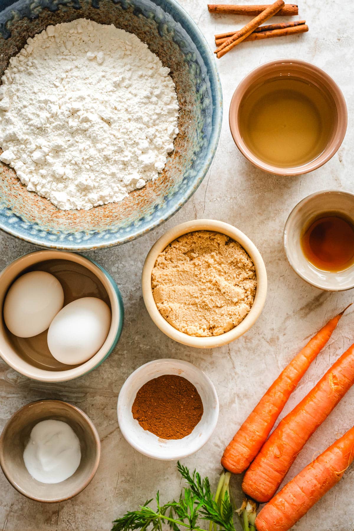 Ingredients for carrot cake cupcakes - flour, eggs, leaveners, warm spices, brown sugar, oil, vanilla extract, and carrots.
